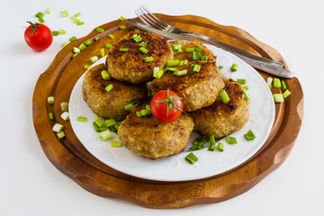 Roasted chicken cutlets with green onion on white plate and small cherry tomatoes on wooden background.