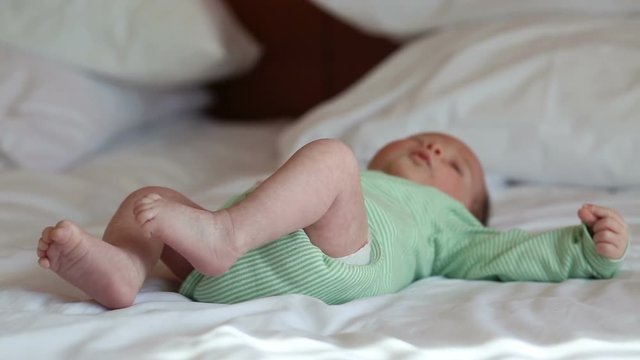 Newborn baby in grey pants lying on a bed