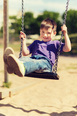 happy little boy swinging on swing at playground