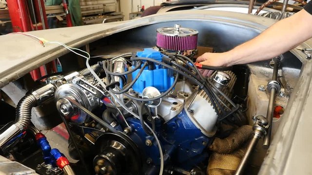 A man starting a race car engine in a shop
