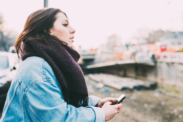 Half length of young beautiful woman leaning on a handrail, holding a smart phone, overlooking pensive - melancholy, serious, thoughtful concept