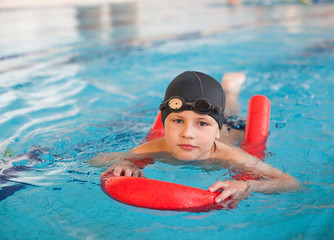 boy learn to swim with  red foam noodle in indoor pool
