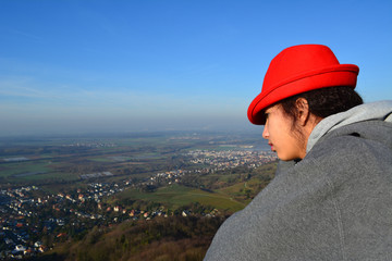Fototapeta na wymiar Lookout One/Girl in red German hat looking down at a city on a sunny day.