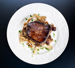 Tasty Beef Mignon steak with mushrooms and herbs on plate.