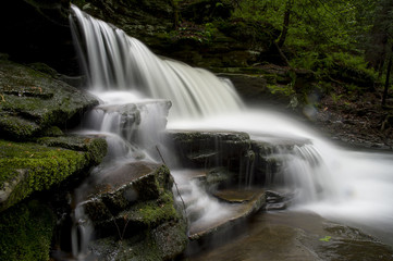 A long exposure of a scenic waterfall landscape in a bright green spring forest.