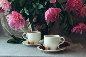 White cup of tea on a background of a vase of peonies..