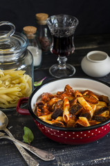Italian pasta with eggplant and tomato sauce and a glass of red wine. On a dark wooden background. Healthy vegetarian food