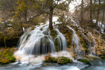 Waterfall in the mountains. The defrost water runs over the rocks. Water flowing over rocks and moss and trees. Water flowing waterfall on a slope