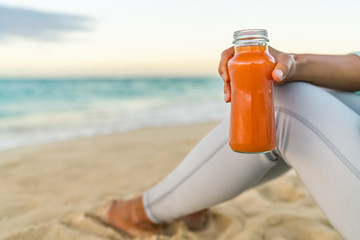 Gezonde wortel groentesap detox reinigen vrouw smoothie drinken voor gewichtsverlies dieet bij strand zonsondergang. Close-up van verse oranje glazen fles. Saptrend, rauw, biologisch en koudgeperst.