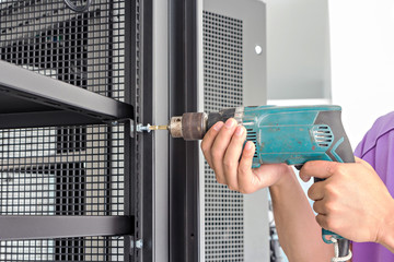 hands hold electric drill on steel cabinet