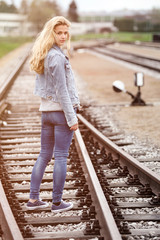 Junge Frau in Jeans-Kleidung blickt auf einem Bahngleis über die Schulter