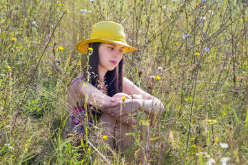 Young girl sitting in the grass, and about something thinks.