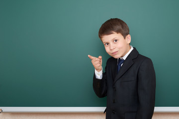 school boy in black suit show finger gesture, on green chalkboard background, education concept