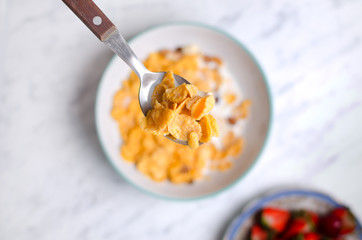 Corn flakes with milk on a spoon and berries pattern on a marble