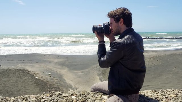 Handome man taking pictures with professional camera in front of the ocean 