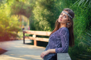 Young female hippie with headband standing in the park with green trees