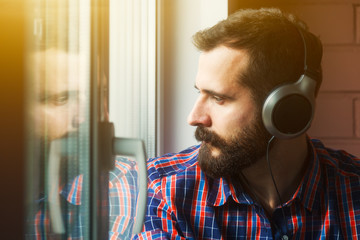 stylish bearded man  in headphones listening to music near windo