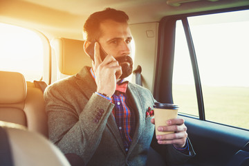 bearded businessman sitting on back seat of car with cup of coff
