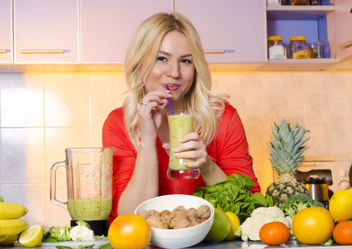 Beautiful young blonde drinking smoothie in her kitchen
