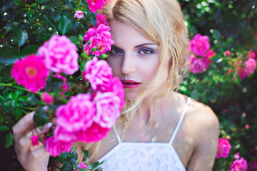 ortrait of young woman near blooming pink rose bush