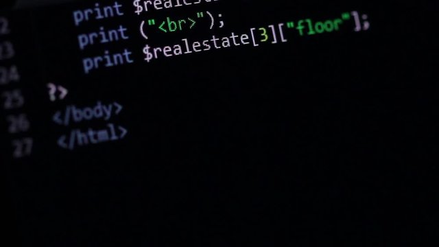 PHP Code scrolling - Computer screen shot under an angle while slowly scrolling a simple PHP code page with realestate related terms and keywords.