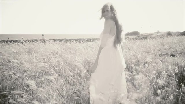 Black and white portrait of woman walking in cornfield in front of ocean