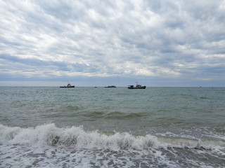 Obraz premium Ships in the sea near the coast, waves and beautiful cloudy sky