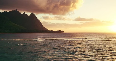 Aerial view flying over ocean reef and waves into dramatic sunset on the north shore of Kauai
