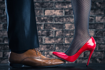 赤いハイヒールの女性が男性の革靴を踏んでいる