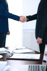 Documents and laptop on the table. Business people shaking hands on the background