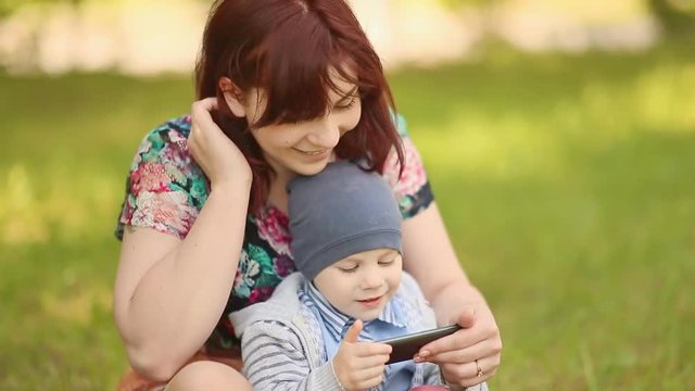Mother and child playing a game with phone on grass