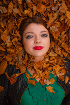 Beautiful young lady is lying between leaves.