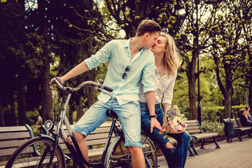 A man on a bicycle kissing cute blond female with flowers.
