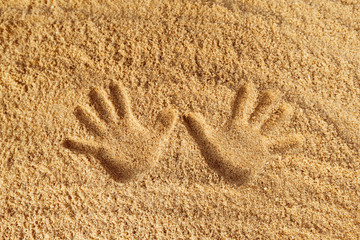 Close-up image of hand prints on yellow textured sand background