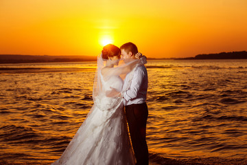 Fototapeta premium Beautiful wedding couple is kissing at golden tropical sunrise 