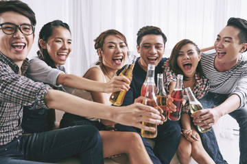 Cheerful Asian young people clinking bottles of beer