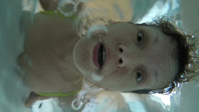 Underwater slow motion of a middle aged female face breathing out air bubbles.