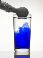 Vibration creates abstract form of blue color in glass of water.
