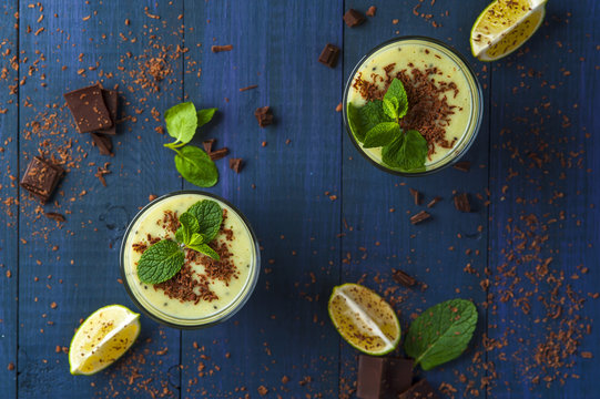 Two glasses of homemade smoothie with kiwi, banana and chocolate flakes, mint leaves and pieces of chocolate on blue rustic background. Conception of healthy food.