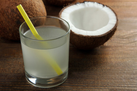 halves of coconut with glass of juice with a cocktail straw on a brown wooden background