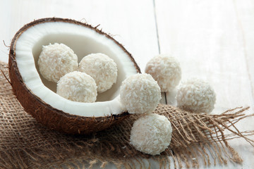 coconut cut into pieces on burlap with candy in coconut chips on a white wooden background
