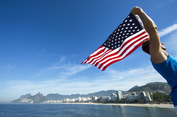 Athlete standing holding American flag above a bright view of the Rio de Janeiro Brazil skyline
