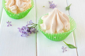 Meringue cake near lilac flowers on the white wooden background