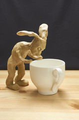 Funny bunny doll sits next to white mug. 