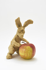 Funny bunny doll sits next to an apple. Shy figure looking at fruit. 