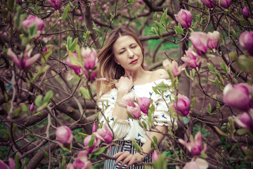 Naklejka premium Young beautiful caucasian woman in blooming spring garden of magnolias . The girl in the garden on a cloudy day .