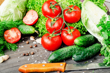 
Fresh juicy ripe summer useful vegetables and greens, red tomatoes , cucumbers , cabbage , lettuce , basil , parsley , dill and salt and spices on a dark wooden background
