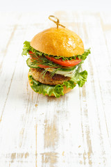 Big beef steak burger with vegetables and herbs on rustic wooden background