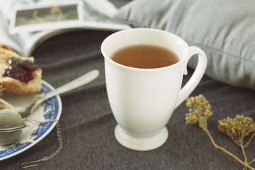 A cup of hot tea with spoon while you take a breakfast with a book and piece of bread