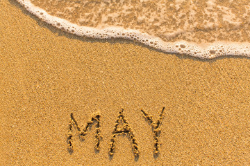 Fototapeta na wymiar May - written by hand on a golden beach sand.